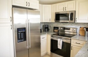 A modern kitchen with stainless steel appliances, white cabinetry, and a granite countertop. - Beautiful and Sweet House Ready for Your Vacation (Sanford)