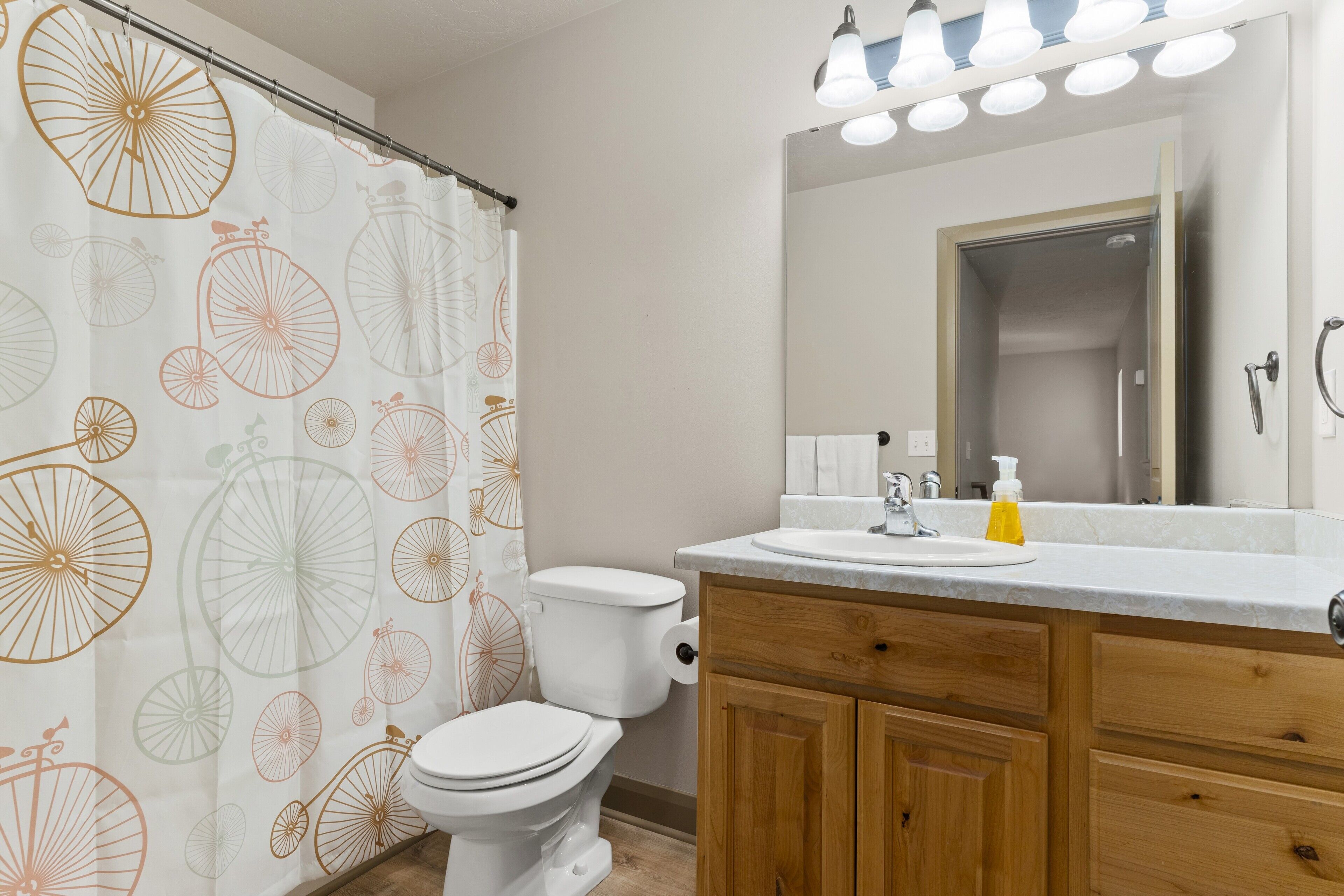 A bathroom with a toilet, wooden cabinets, a sink with a mirror, and a shower curtain with bicycle patterns.