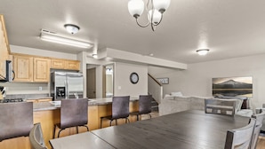 A modern kitchen with wooden cabinets, a stainless steel refrigerator, and a dining area with a large wooden table and chairs. - Willow Park House on Fairway Ln (Logan)