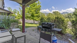 An outdoor patio with a grill, seating, and a view of a green landscape. - Willow Park House on Fairway Ln (Logan)