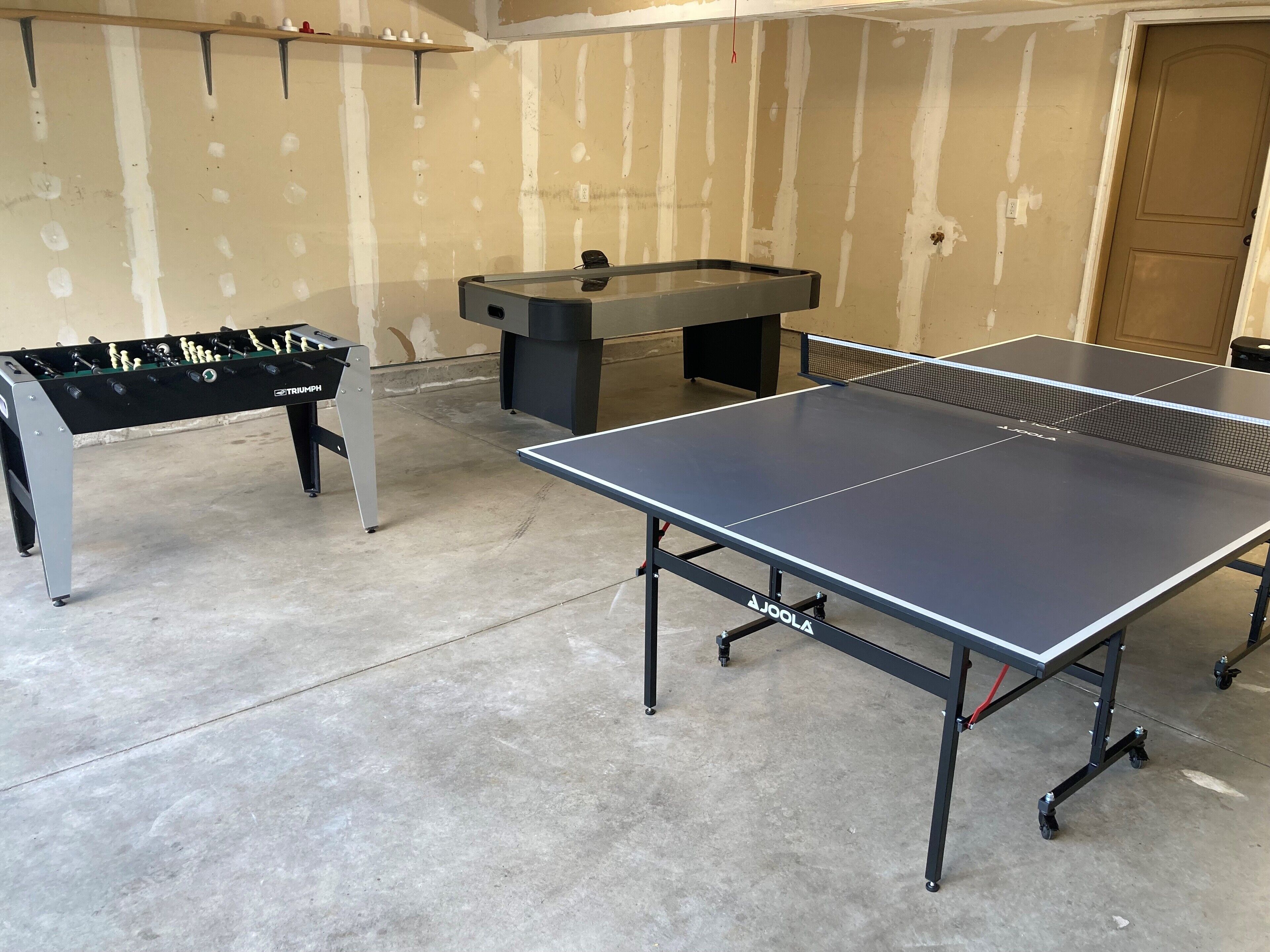 Una stanza con un tavolo da calcio, un tavolo da ping pong e un tavolo da tennis.