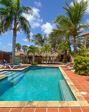 A swimming pool with clear blue water, surrounded by palm trees and a tiled walkway. - Boutique Hotel Sonrisa Bonaire - Adults Only (Kralendijk)