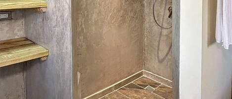A walk-in shower with a tiled floor and wooden shelves.