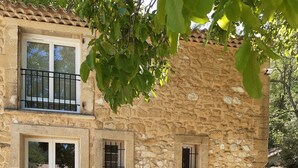 A stone building with a balcony, a dining area with a table and chairs, and a grill outside.