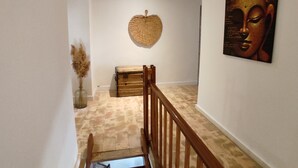 A staircase with a wooden railing, a woven wall hanging, and a Buddha painting.