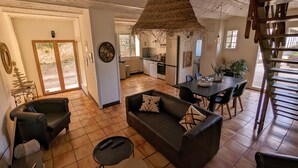 A spacious living area with a sofa, a coffee table, and a dining table. There is a kitchen in the background with a refrigerator and a stove.