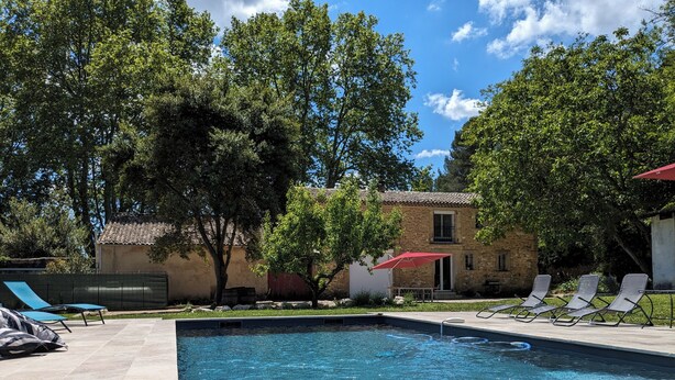 A rectangular swimming pool with a wooden deck, surrounded by lounge chairs and a stone building.