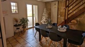A dining area with a black table, chairs, and a Christmas tree. There is a staircase with wooden railings and a view of the outside.