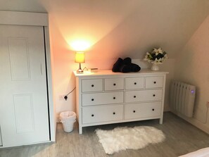 A white dresser with drawers, a lamp, a basket, and a radiator.