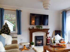 Una sala de estar con chimenea, televisor, árbol de Navidad y una mesa de comedor con fruta.