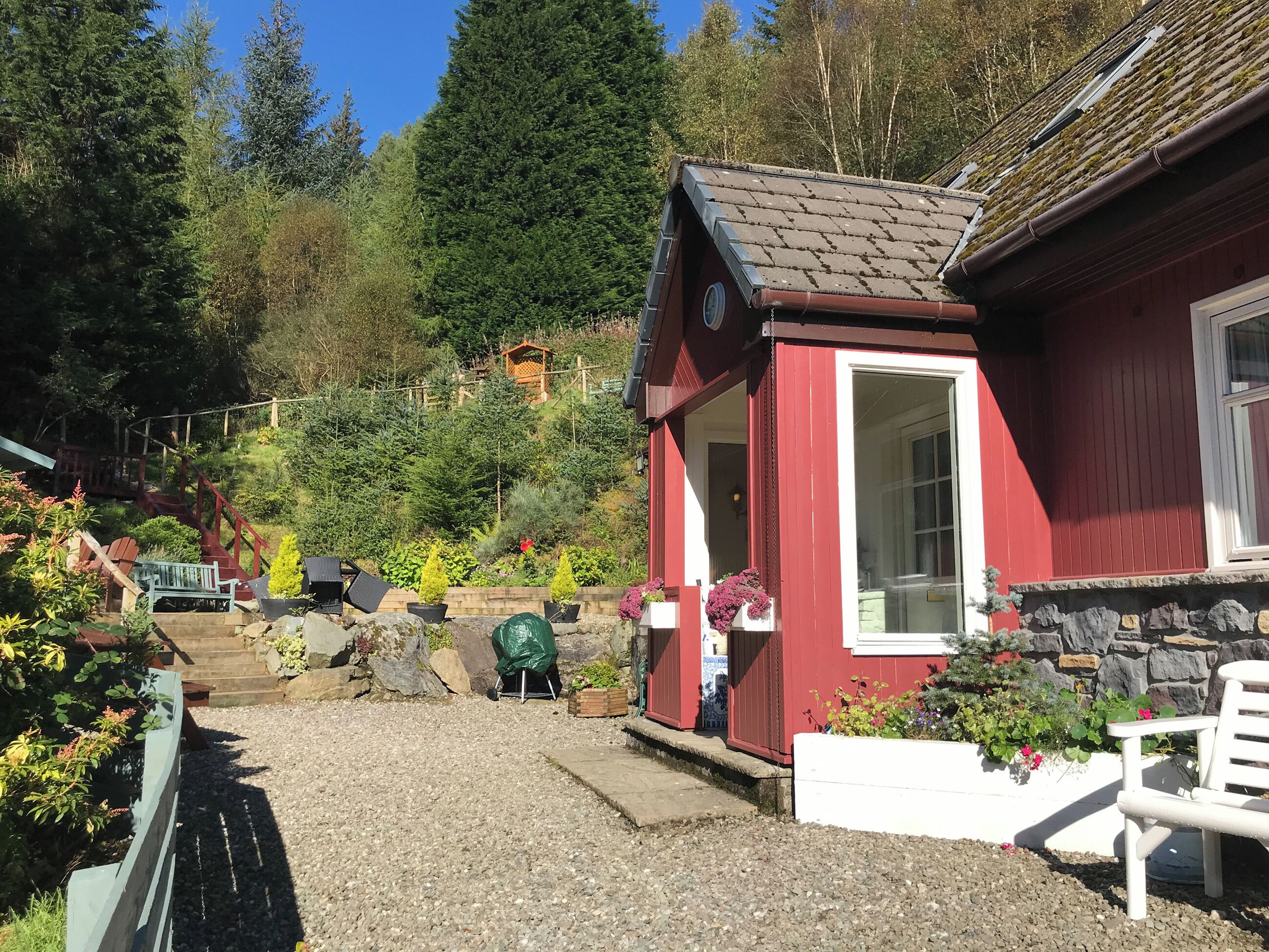 En röd byggnad med en liten veranda, en stenmur och en grusgång som leder till en trätrappa.