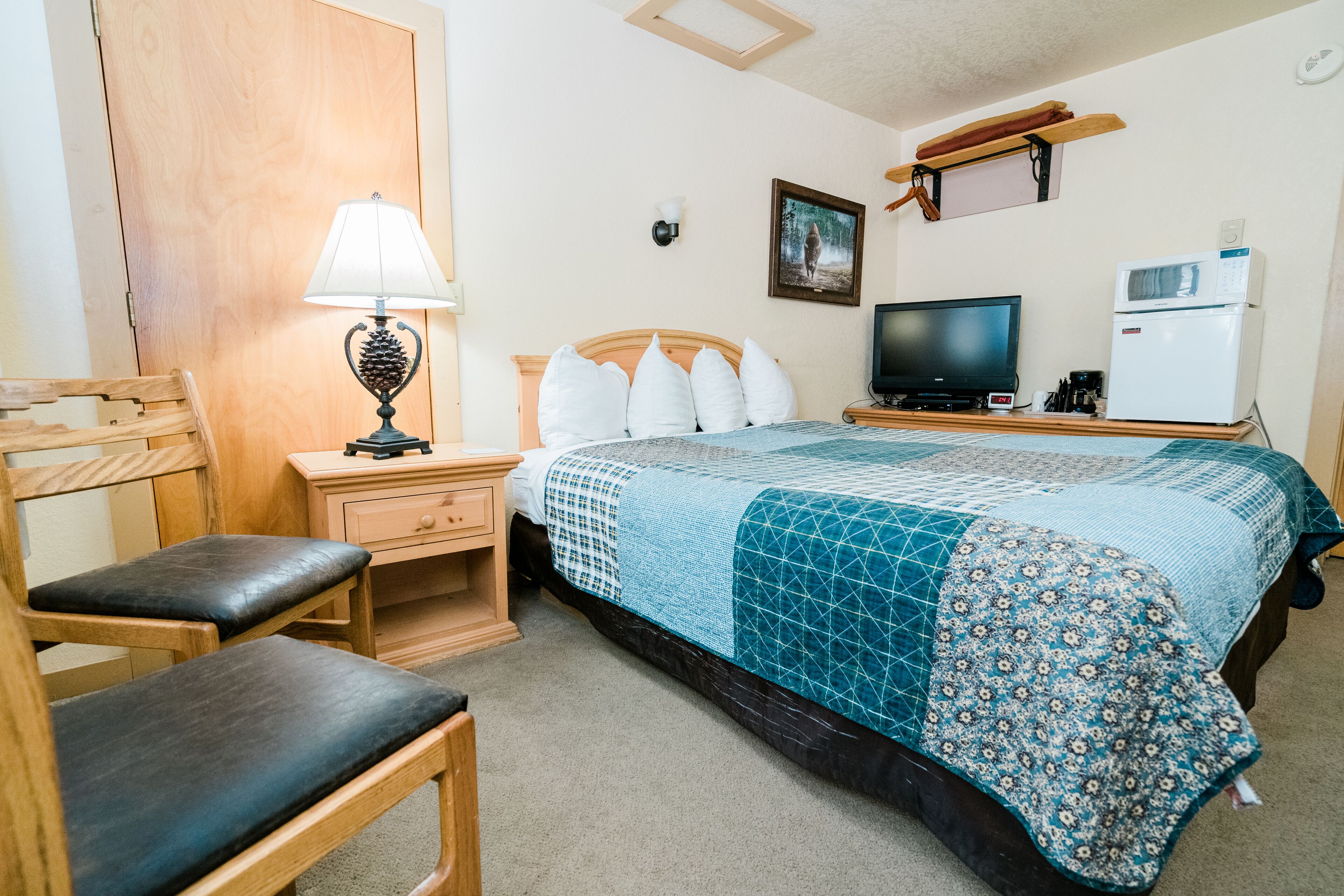 A bedroom with a bed, a desk, a chair, a lamp, a television, and a refrigerator.