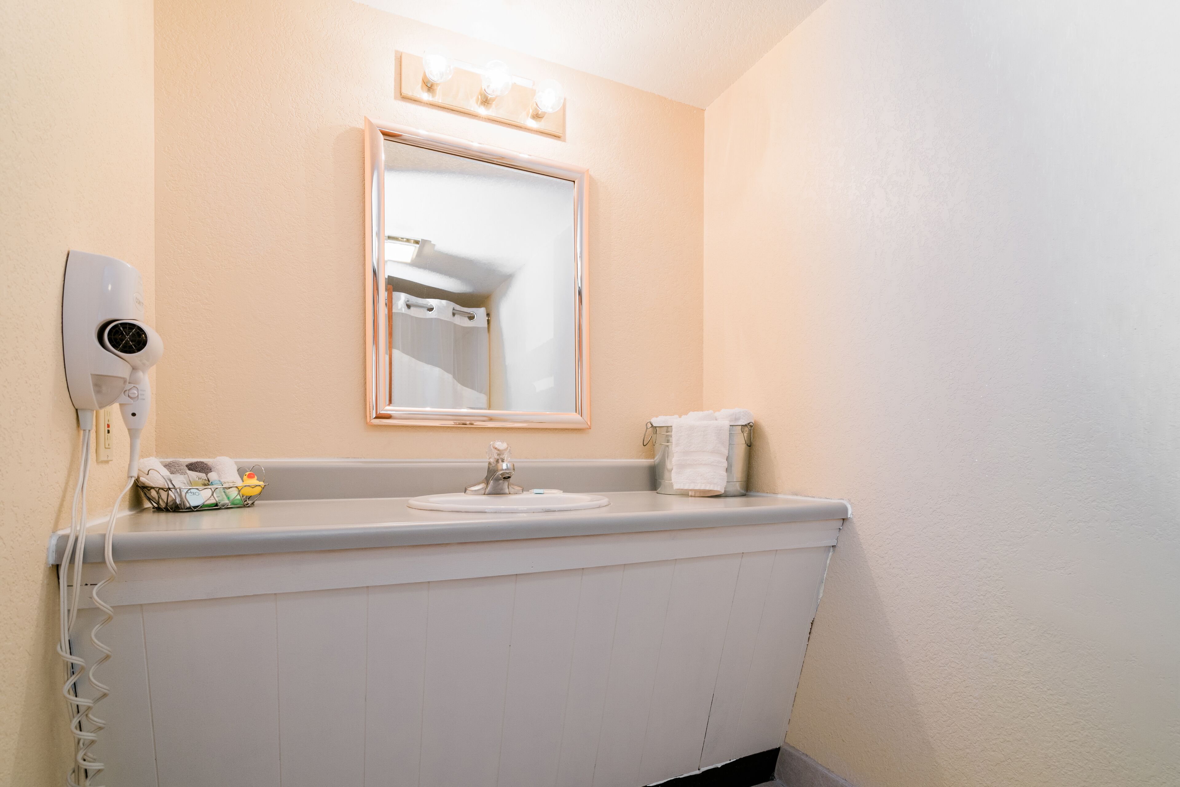 Un baño con lavamanos, espejo, secador de pelo y toallero.