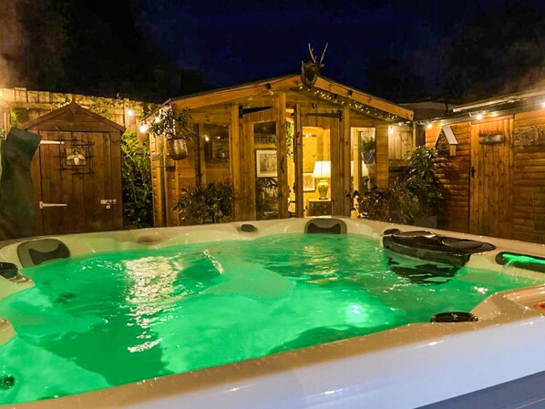 A wooden cabin with a hot tub, a wooden door, and a small shed.