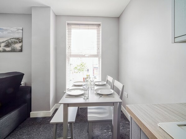 Un comedor con una mesa preparada para cuatro, un banco y una ventana con persianas.