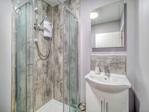 Ein modernes Badezimmer mit einer gläsernen Dusche, einem weißen Waschbecken und einem Spiegel darüber.