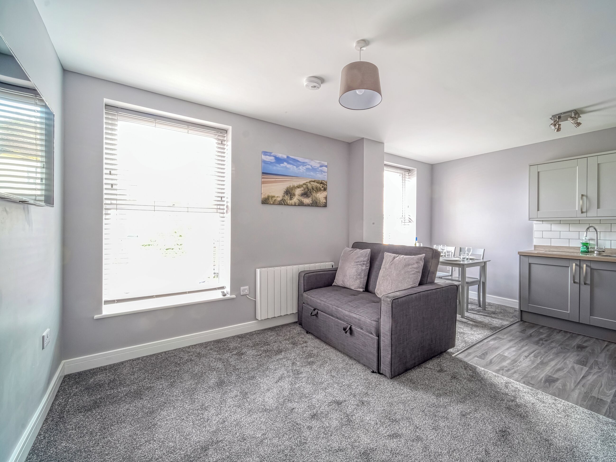 A modern, compact living space with a grey sofa, a dining table, and a kitchen area.