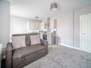 Un espacio habitable compacto con un sofá gris, una kitchenette y una puerta blanca.