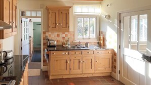 Une cuisine avec des meubles en bois, un grand îlot central, une cuisinière et une fenêtre avec des stores.