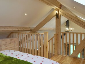 A loft bedroom with a wooden staircase, a bed with a white and green bedspread, and a chandelier.