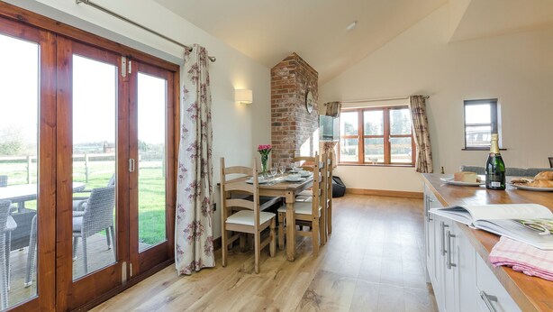 A dining area with a wooden table, chairs, and a bottle of champagne. - Tawny Cottage - UKC2580 (Yoxall, near Lichfield)