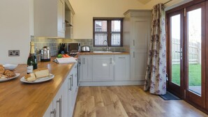 A modern kitchen with white cabinets, a wooden countertop, a sink, and a window with blinds. - Tawny Cottage - UKC2580 (Yoxall, near Lichfield)