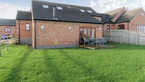 A brick building with a sloped roof and skylights, a wooden fence, and a grassy yard with outdoor furniture. - Tawny Cottage - UKC2580 (Yoxall, near Lichfield)