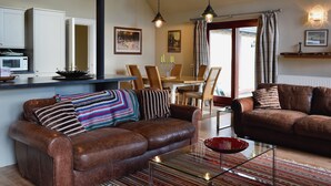 Een woonkamer met een bruine leren bank, een glazen salontafel en een eethoek met een houten tafel en stoelen.
