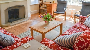 A living room with a fireplace, a TV, a coffee table with a vase of flowers, and two armchairs.