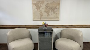 Ein Zimmer mit zwei beigen Sesseln, einem kleinen Tisch mit Weltkarte und einer Glasvitrine mit Wasserflaschen.