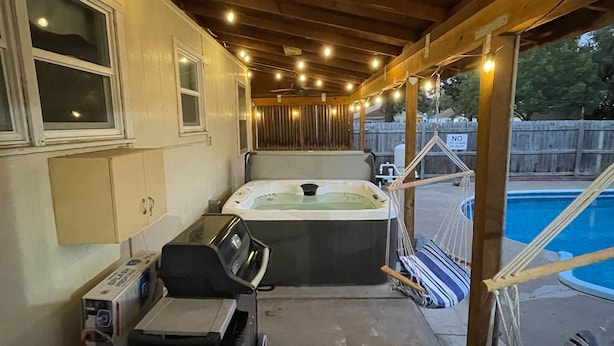 Ein überdachter Patio-Bereich mit Whirlpool, Grill und Pool.