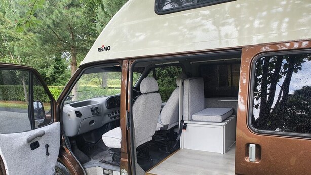 A camper van interior with a kitchenette, seating area, and a small table. - Camper 8 “Bertha” (Leinster)