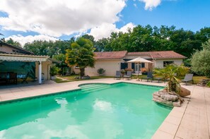 A swimming pool with a tiled deck, lounge chairs, and a covered patio area.