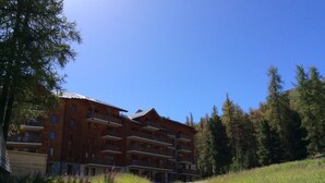 A multi-story building with balconies, surrounded by trees and a gravel path. - Appartement T2 Albane Vars (vars)