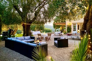 An outdoor seating area with a sofa, chairs, and tables, surrounded by trees and a view of the countryside.