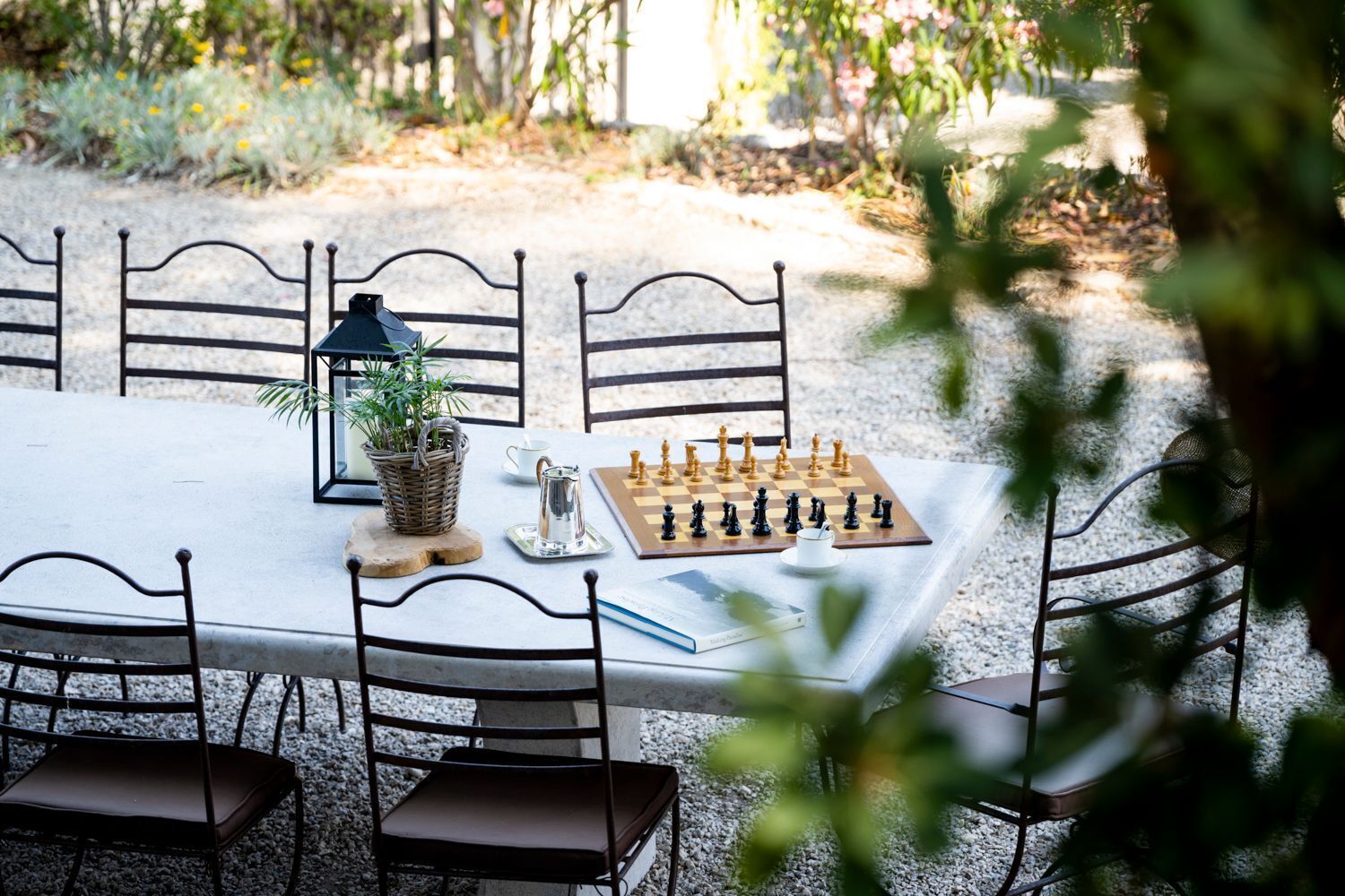 An outdoor dining area with a chessboard, chairs, a table, a plant, and a pitcher.