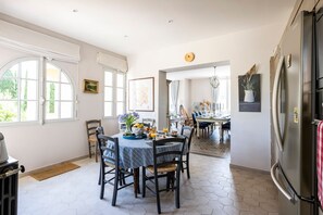 A spacious kitchen with a dining area, featuring a large refrigerator, a dining table set for four, and a view of the adjacent dining room.