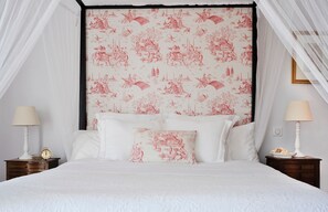 A bed with a canopy and a patterned headboard, two bedside tables with lamps, and a clock on one of the tables.