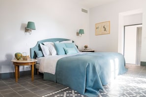 A bedroom with a bed, two bedside tables, a wall-mounted lamp, a framed picture, and a patterned floor.