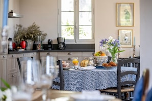 A breakfast table set with a patterned tablecloth, a vase of flowers, and various breakfast items.