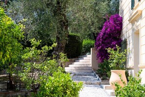 Un jardin avec un escalier en pierre menant à un bâtiment, le tout entouré de verdure et de fleurs violettes.