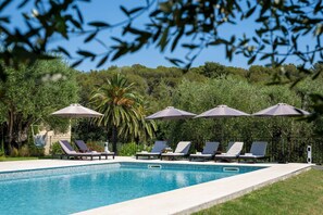 A swimming pool with lounge chairs and umbrellas, surrounded by greenery.