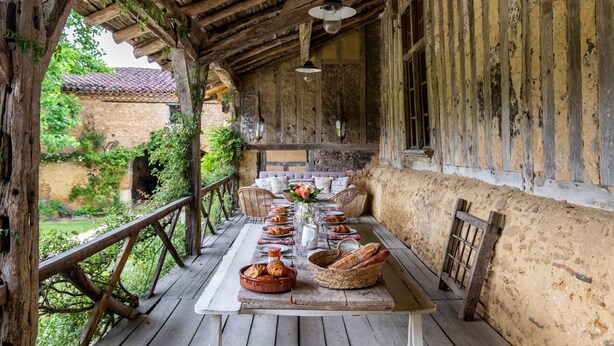 A rustic wooden table set with bread and pastries on a wooden deck with a view of greenery and a building in the background. - Manoir Gascon - Five Bedroom Villa, Sleeps 12 (Estang)