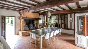 A rustic kitchen with exposed wooden beams, a brick fireplace, and a dining area with a large table and white chairs. - Manoir Gascon - Five Bedroom Villa, Sleeps 12 (Estang)