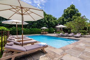 A swimming pool with lounge chairs and umbrellas, surrounded by stone tiles and greenery.
