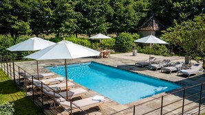A rectangular swimming pool with lounge chairs and umbrellas, surrounded by a stone deck and lush greenery. - Manoir Gascon - Five Bedroom Villa, Sleeps 12 (Estang)