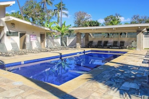 A swimming pool with lounge chairs and a covered area, surrounded by palm trees and a clear sky.