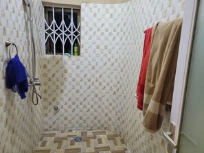 A shower area with a tiled wall, a window with bars, and a towel rack with towels.