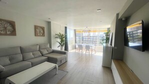 Ein modernes Wohnzimmer mit einem grauen Sofa, einem weißen Couchtisch und einem Essbereich mit Tisch und Stühlen.
