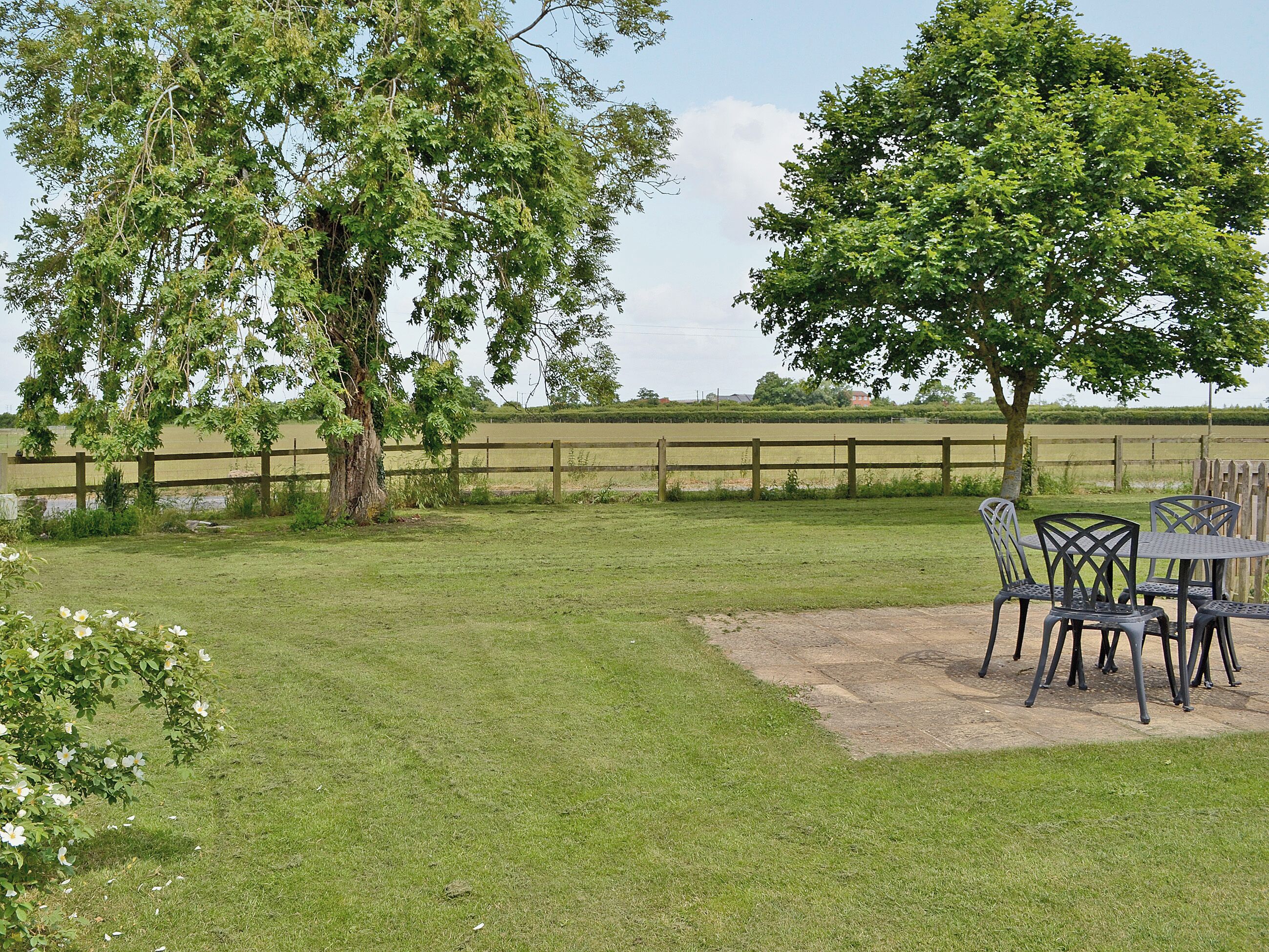 A grassy outdoor area with a table and chairs, a wooden fence, and trees.
